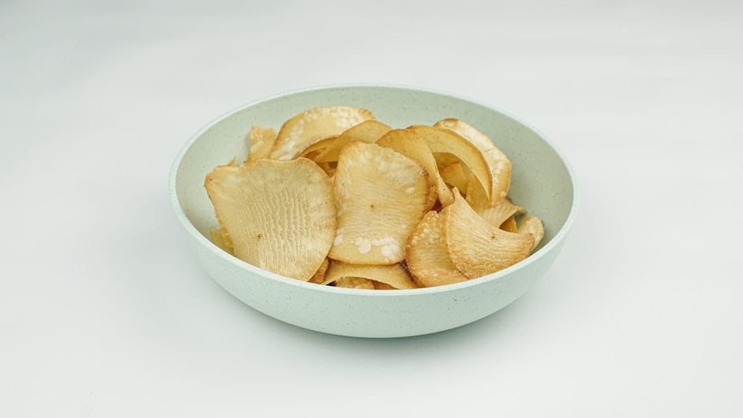 Plain potato crisps piled in a pale ceramic bowl on white