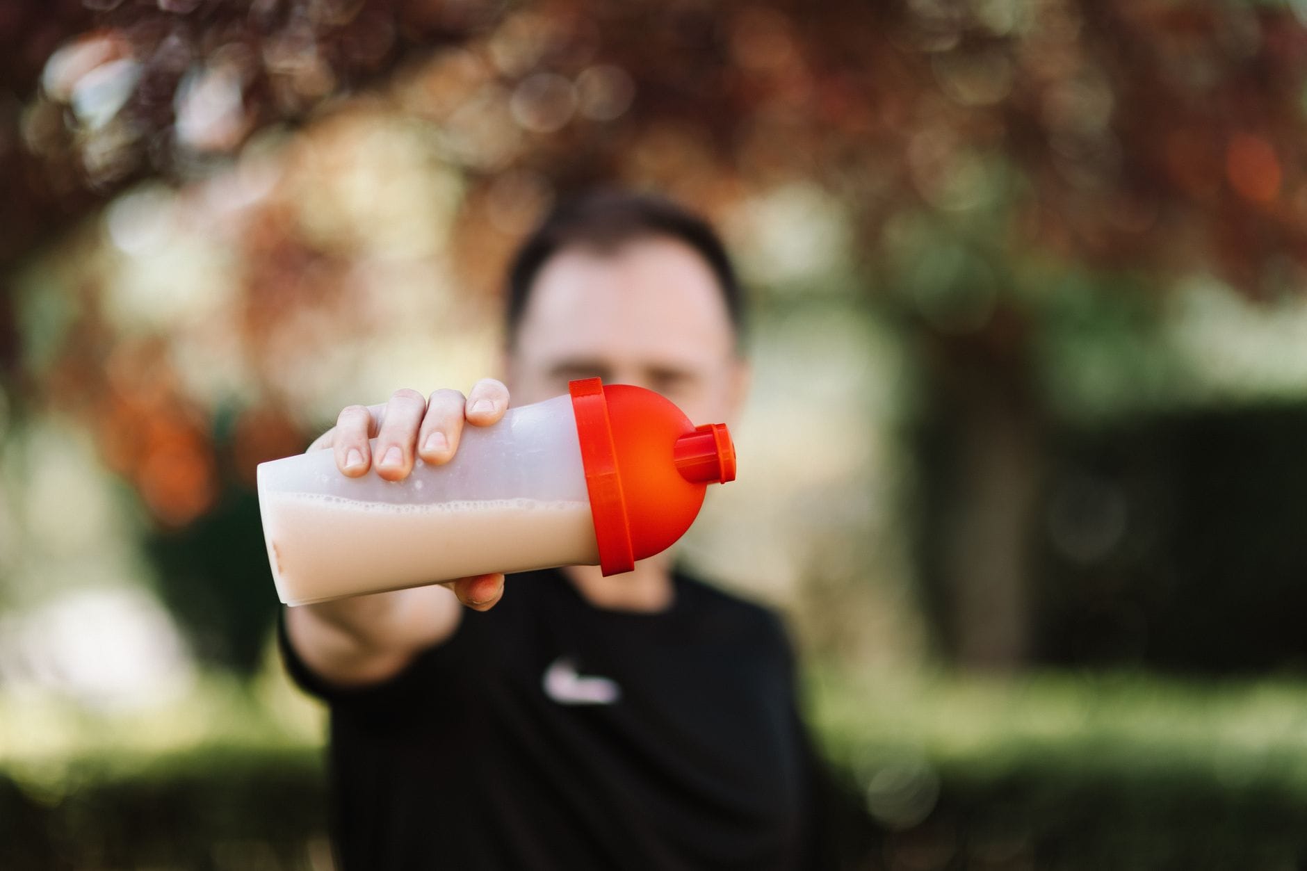 Man holding a plastic shaker tumbler of protein drink outdoors