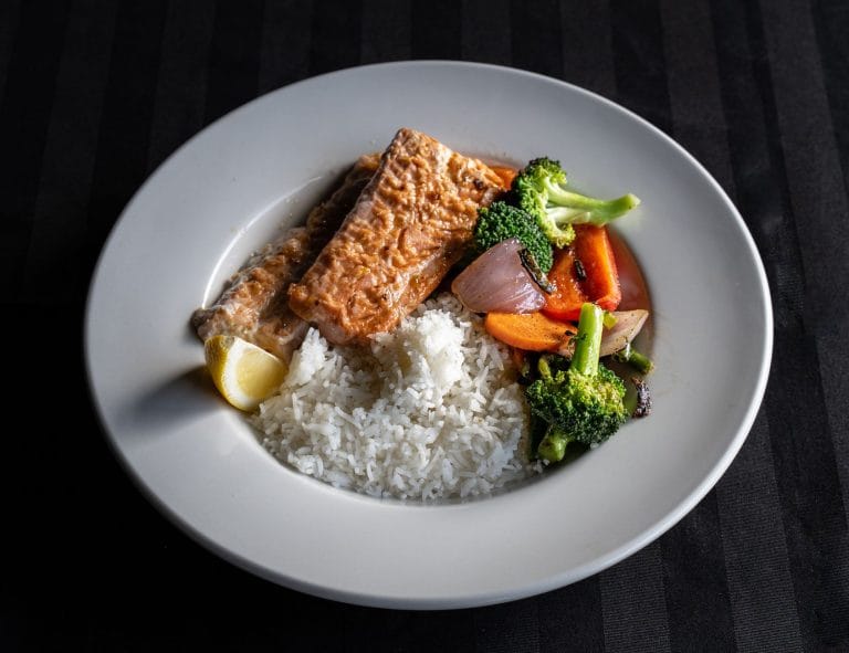 Plate of cooked salmon with white rice, broccoli, carrot and red onion