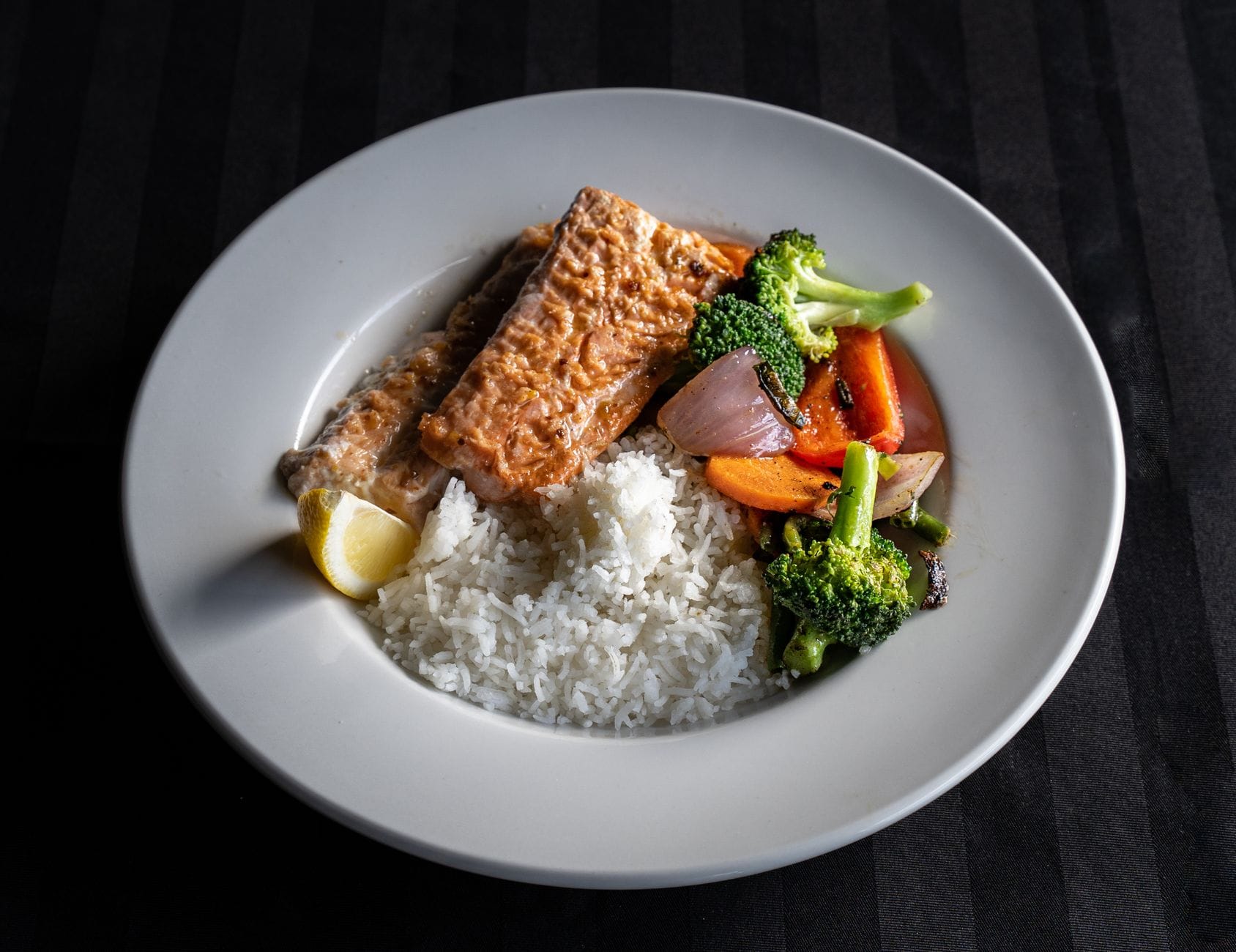 Plate of cooked salmon with white rice, broccoli, carrot and red onion