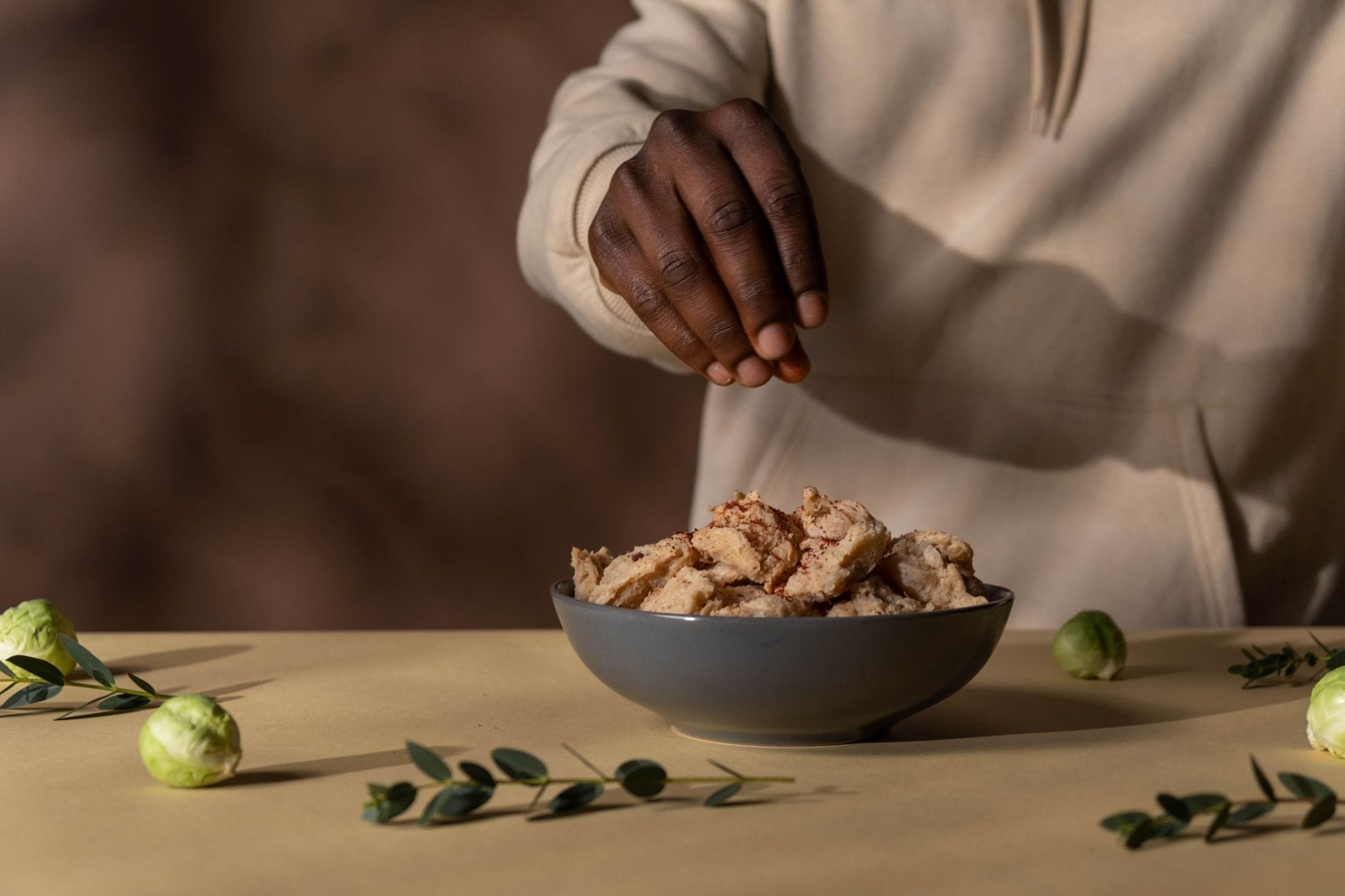 Hands seasoning a bowl of cooked plant-based protein chunks