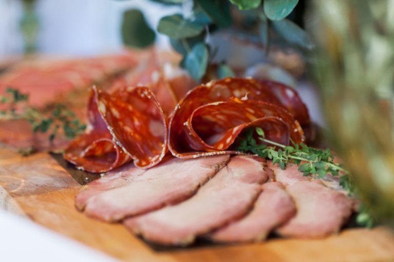 Slices of salami and cured ham arranged on a wooden board with sprigs of thyme
