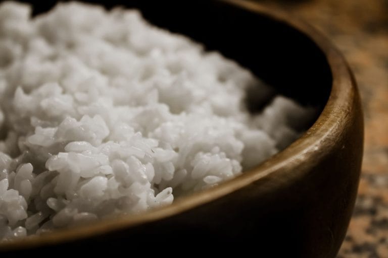 Close-up of steamed white rice in a dark wooden bowl