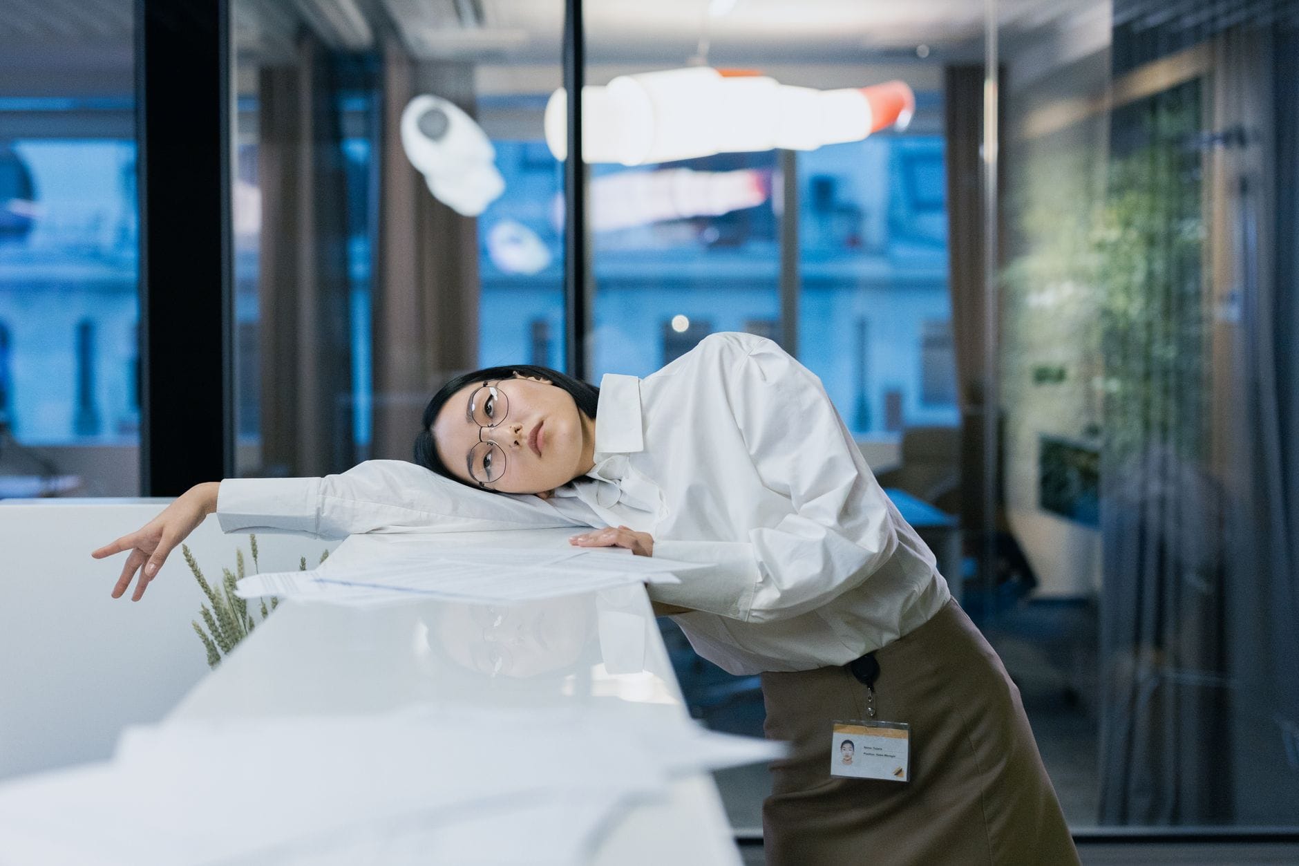 Exhausted office worker in a white shirt slumped sideways across a desk covered in papers
