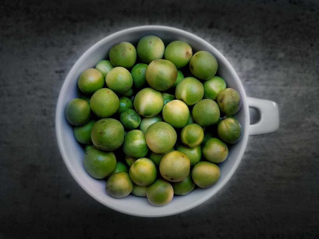 Green turkey berries (Solanum torvum) piled in a white cup on a dark surface