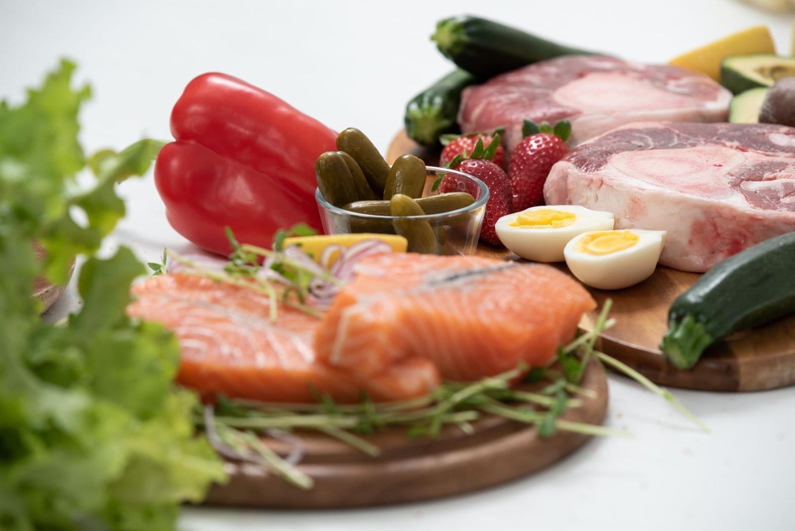 Raw salmon fillets, halved boiled eggs and raw beef chops on wooden boards with vegetables