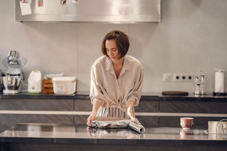 Person covering a baking tray with aluminum foil on a dark kitchen island
