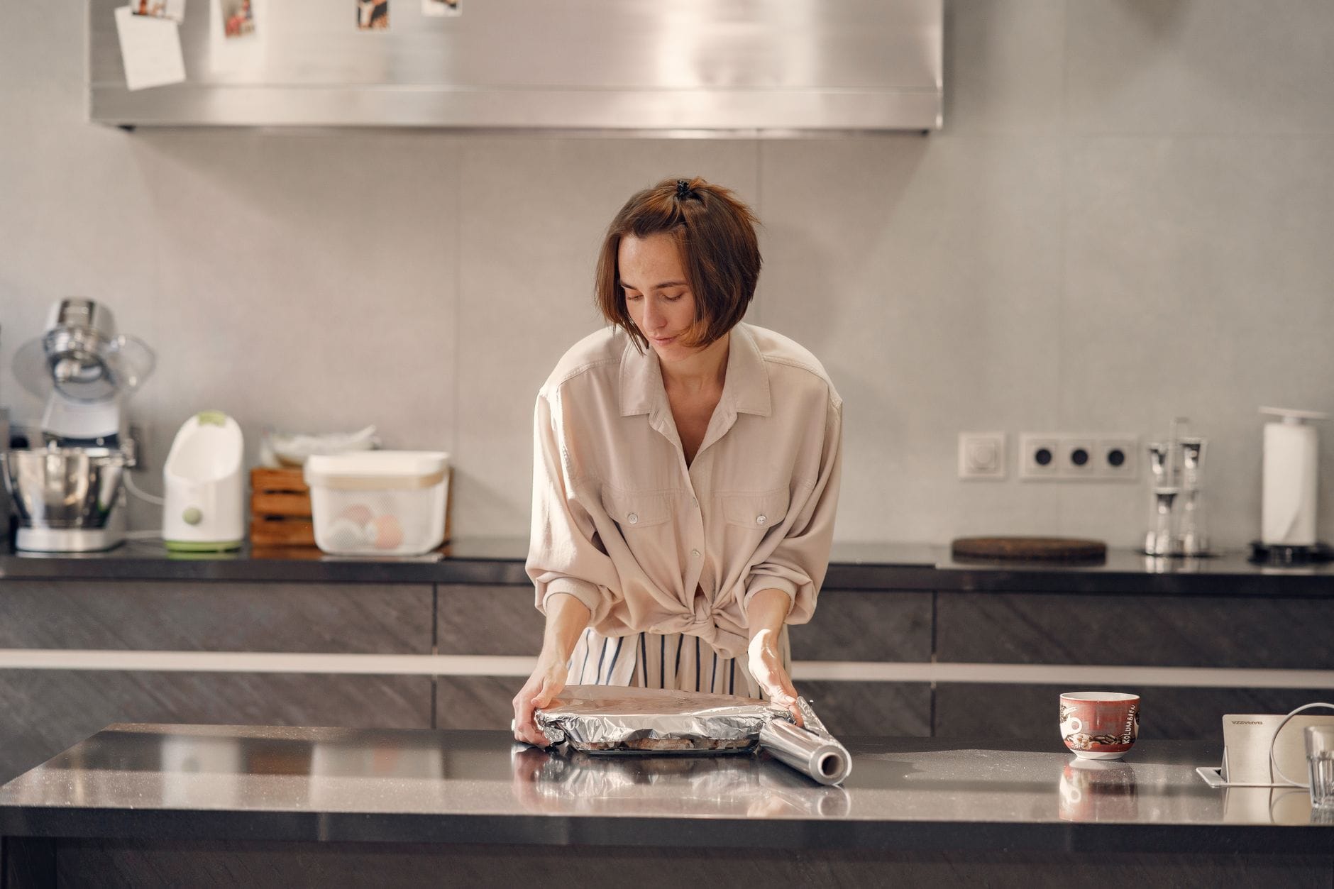 Person covering a baking tray with aluminum foil on a dark kitchen island