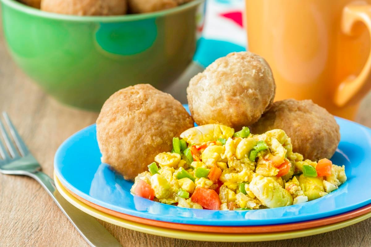 Plate of ackee and saltfish with fried dumplings and a mug on a wooden table