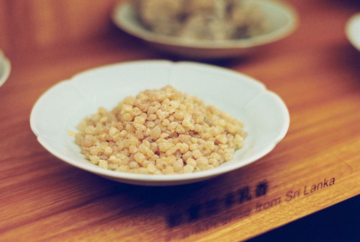 Pale frankincense resin granules heaped in a small white dish on a wooden counter