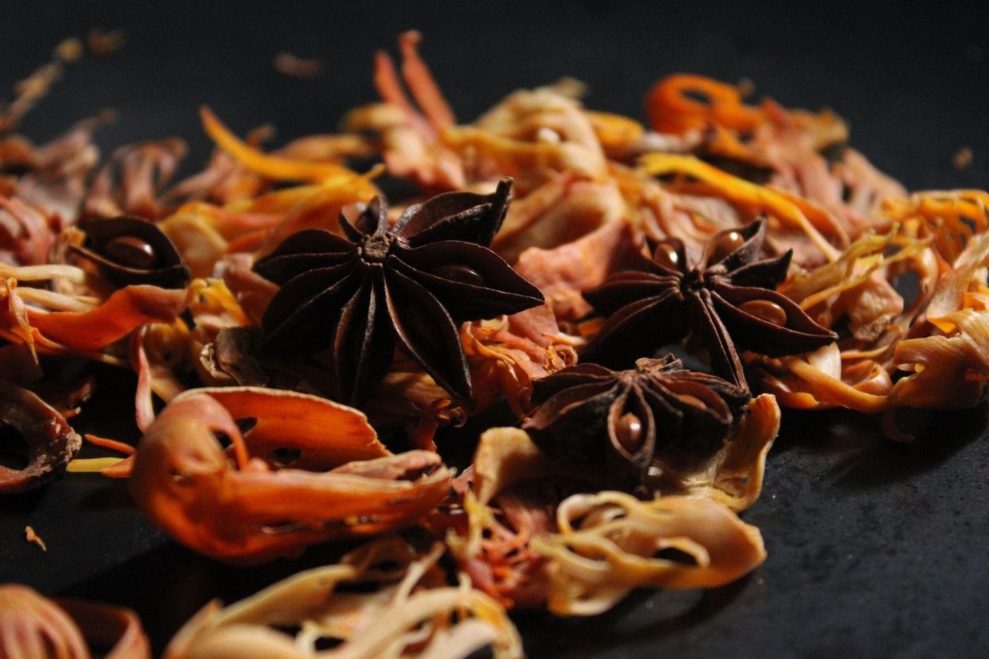 Dried mace blades, flat and orange-tan, mixed with star anise on a dark surface