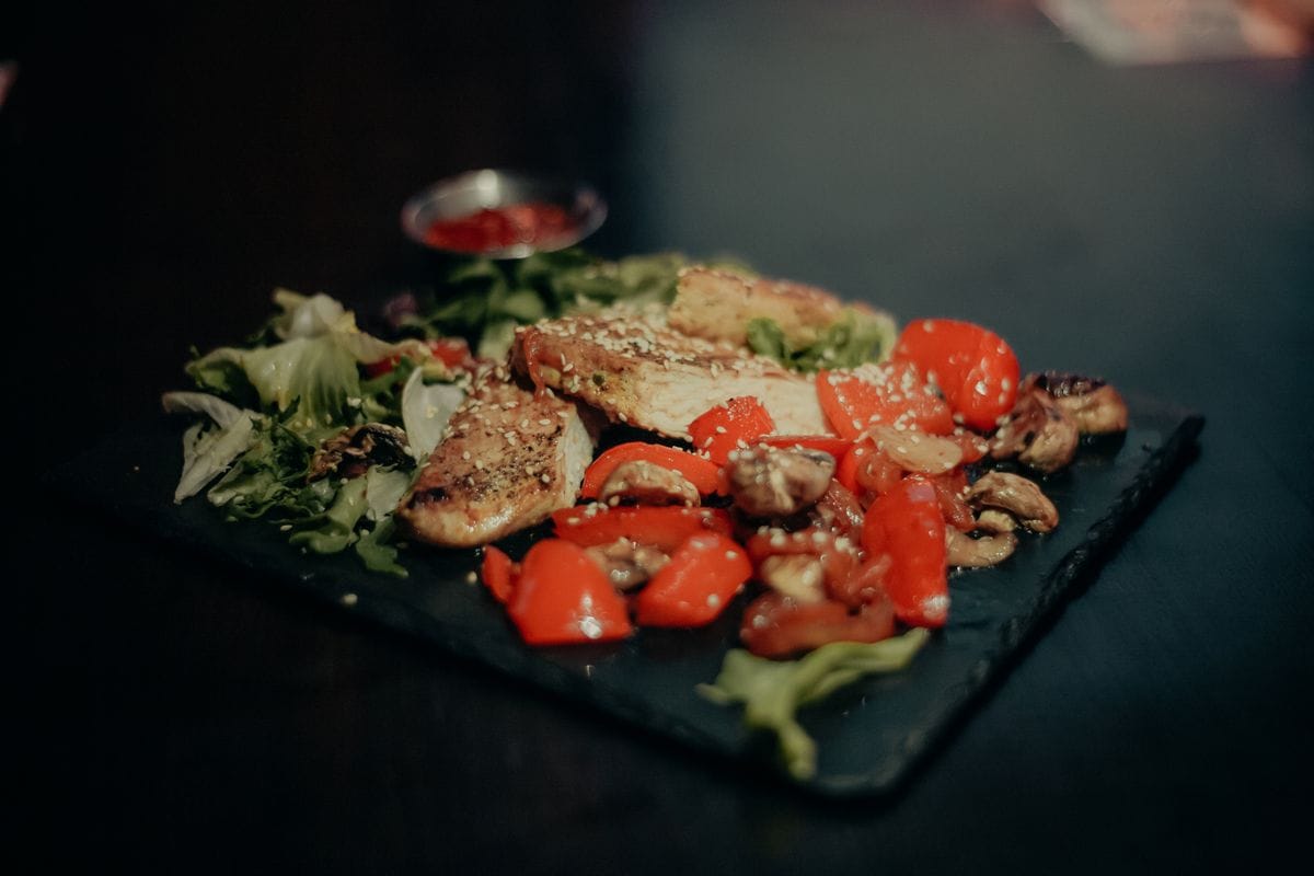Grilled chicken breast with sauteed onions, broccoli, carrot, tomato and lettuce on a white plate