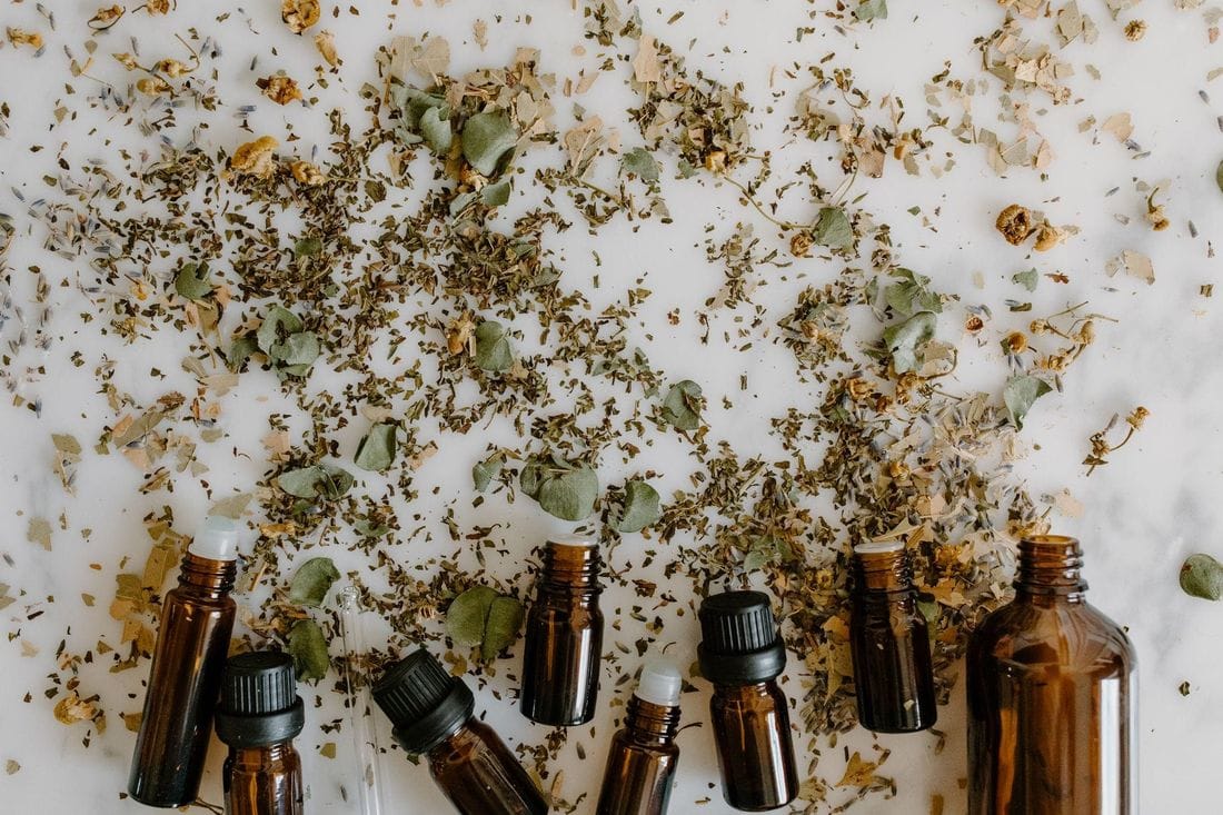 Unlabelled amber essential oil bottles among scattered dried herbs and flowers