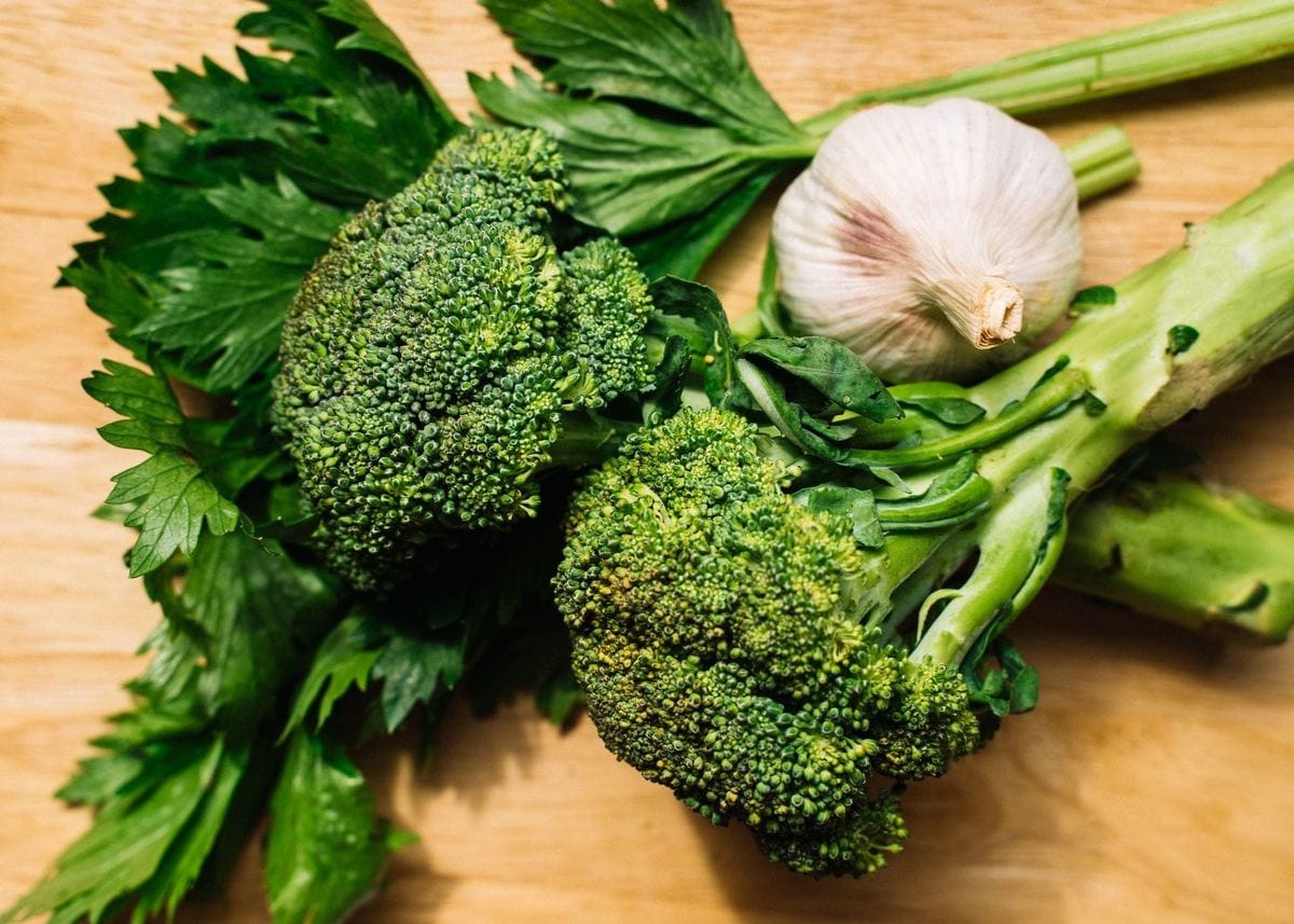 Broccoli heads, flat-leaf parsley and a bulb of garlic on a wooden board